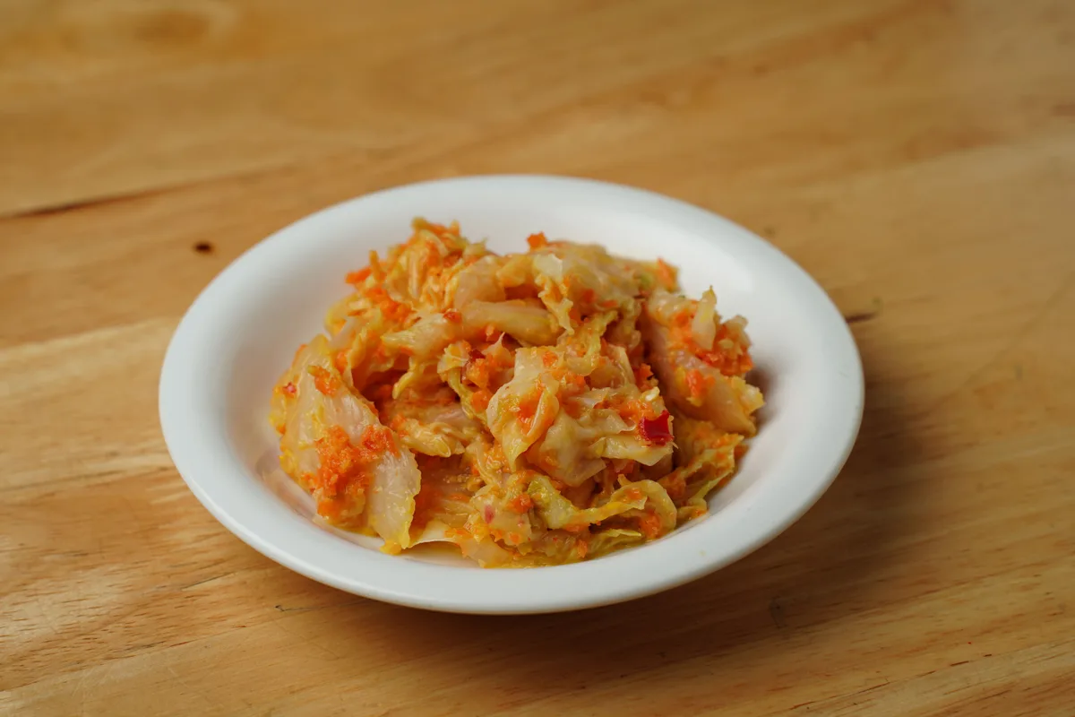 A small white plate of shredded cabbage kimchi on a wooden table