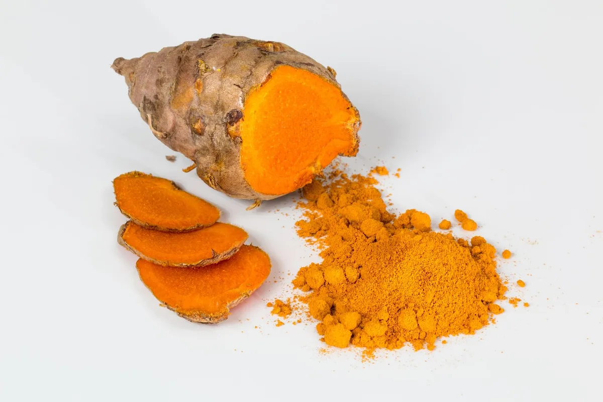 A fresh turmeric root cut open to show its bright orange flesh, with slices and a pile of ground turmeric