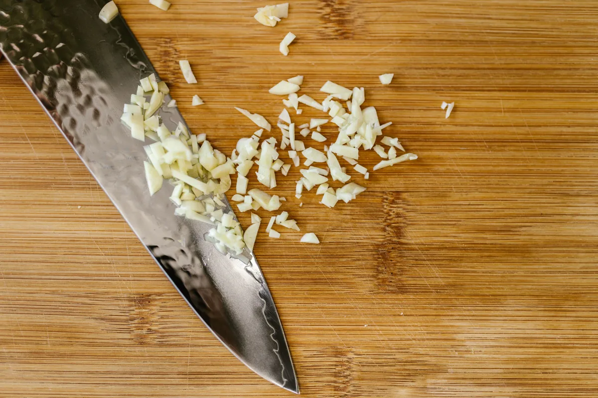 Minced garlic on a wooden cutting board beside the blade of a chef's knife