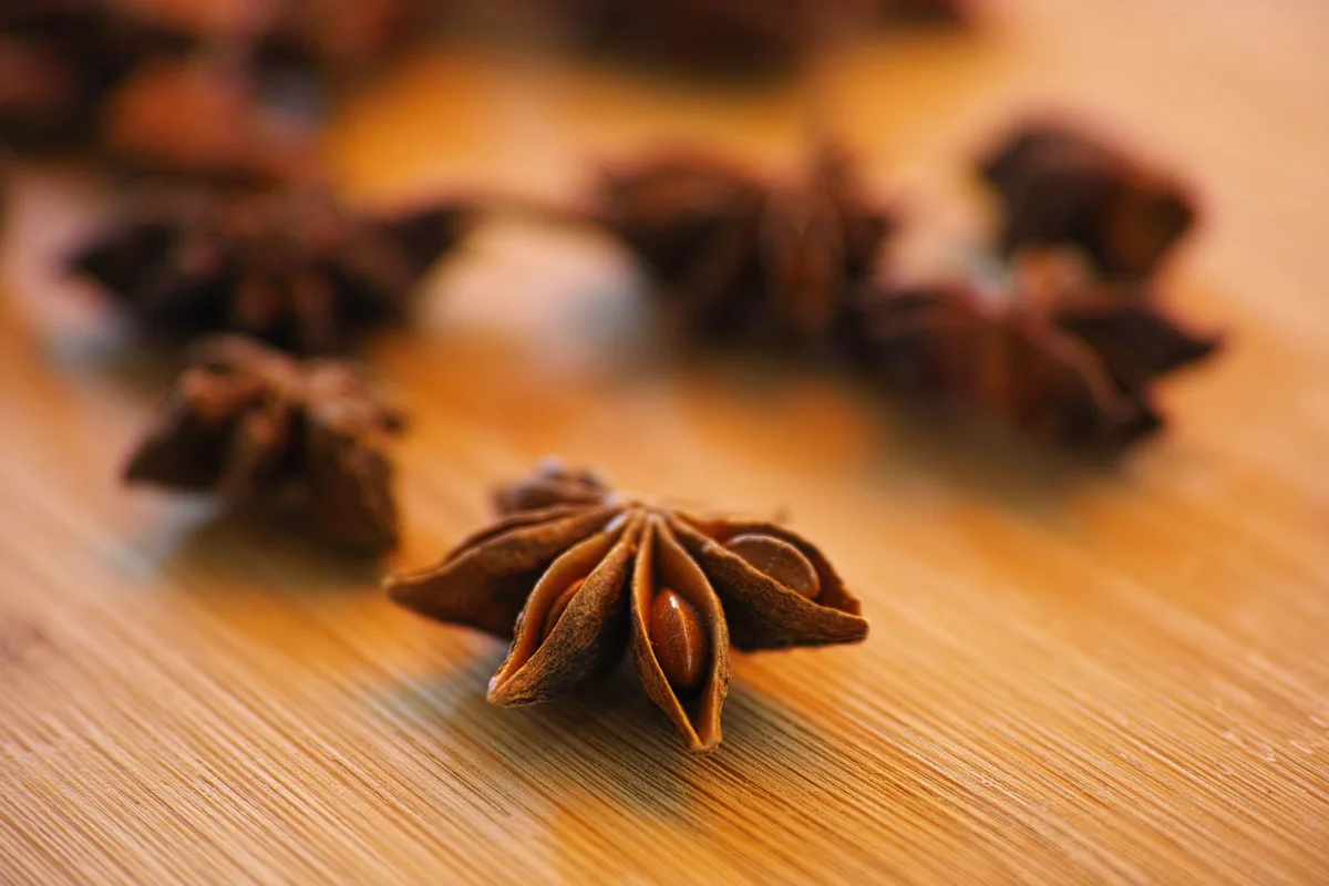 Whole star anise pods on a wooden surface, one in sharp focus