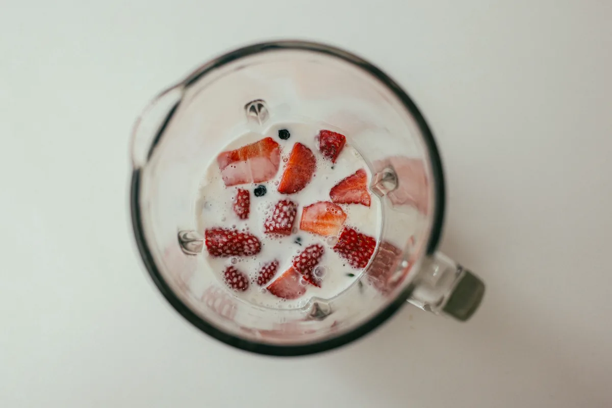 Sliced strawberries and milk in a blender jug, seen from above