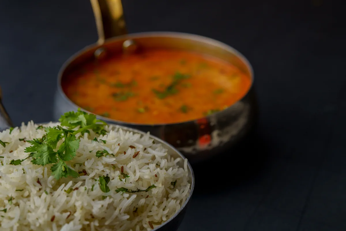 A pan of yellow dal next to a bowl of cumin rice topped with cilantro