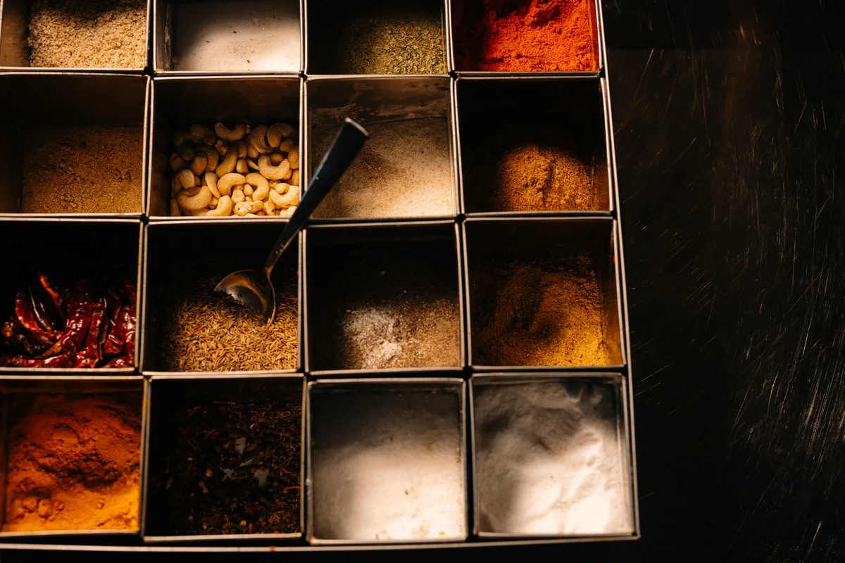 A steel box divided into square compartments of ground spices, dried red chilies and cashews