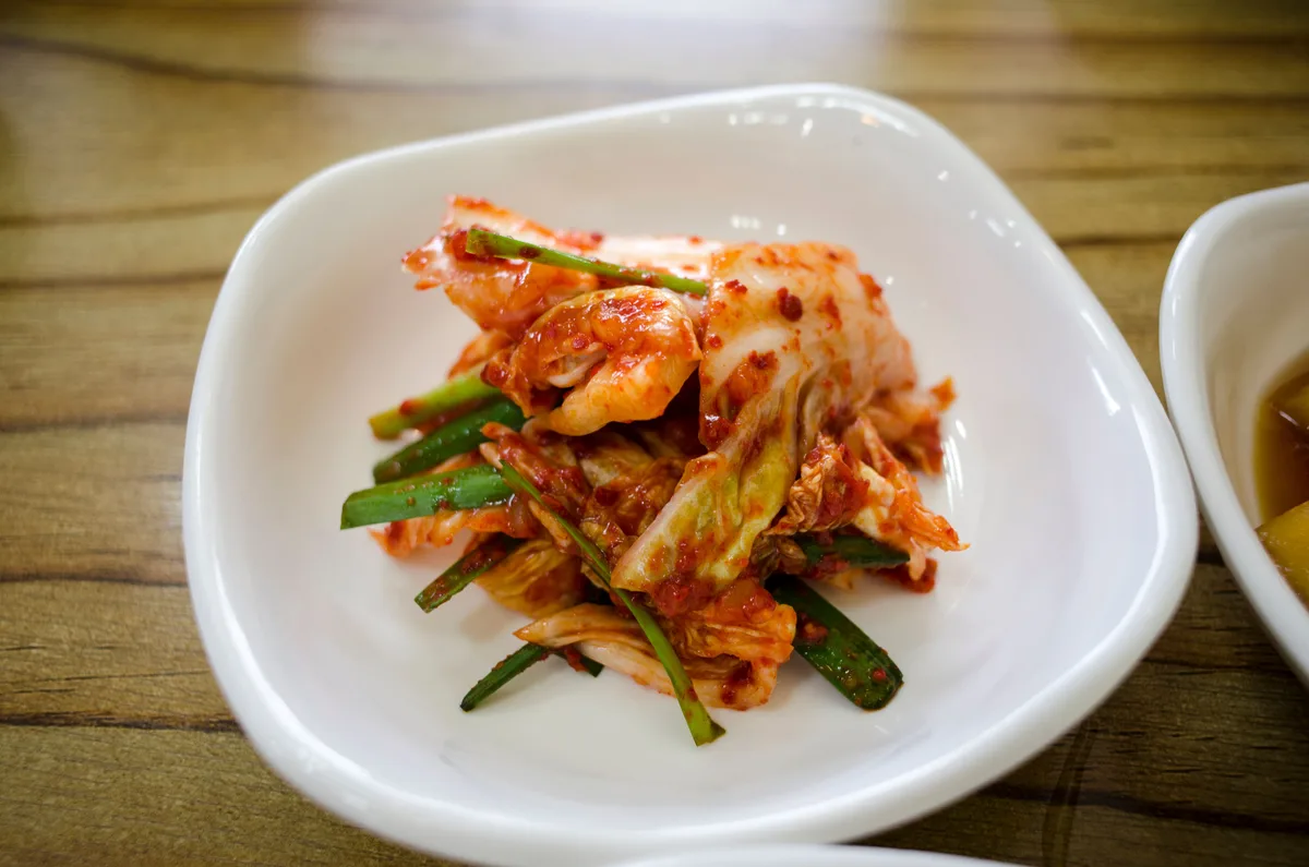 Napa cabbage kimchi with scallions in a white dish