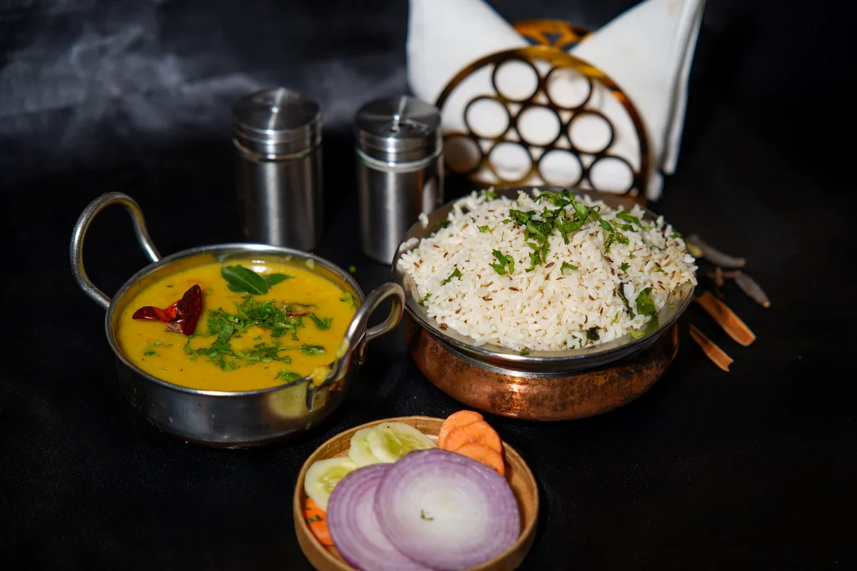 A bowl of yellow dal beside cumin rice and a dish of sliced onion