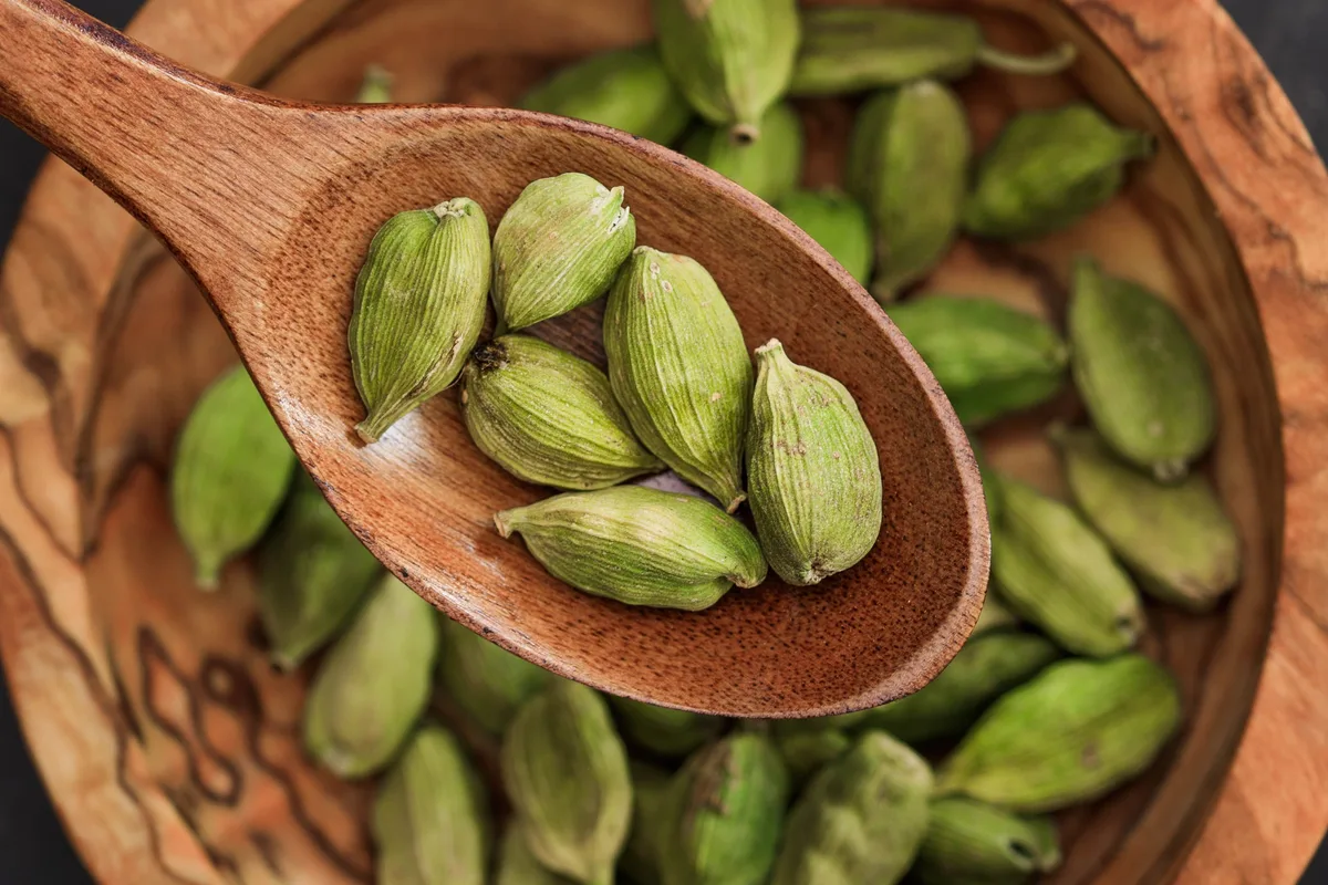 Green cardamom pods in a wooden spoon and bowl