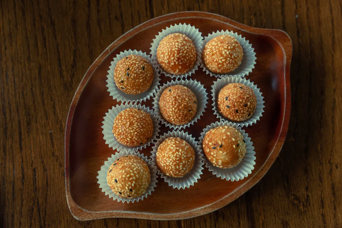 Sesame-coated sweet balls in paper cases on a wooden dish