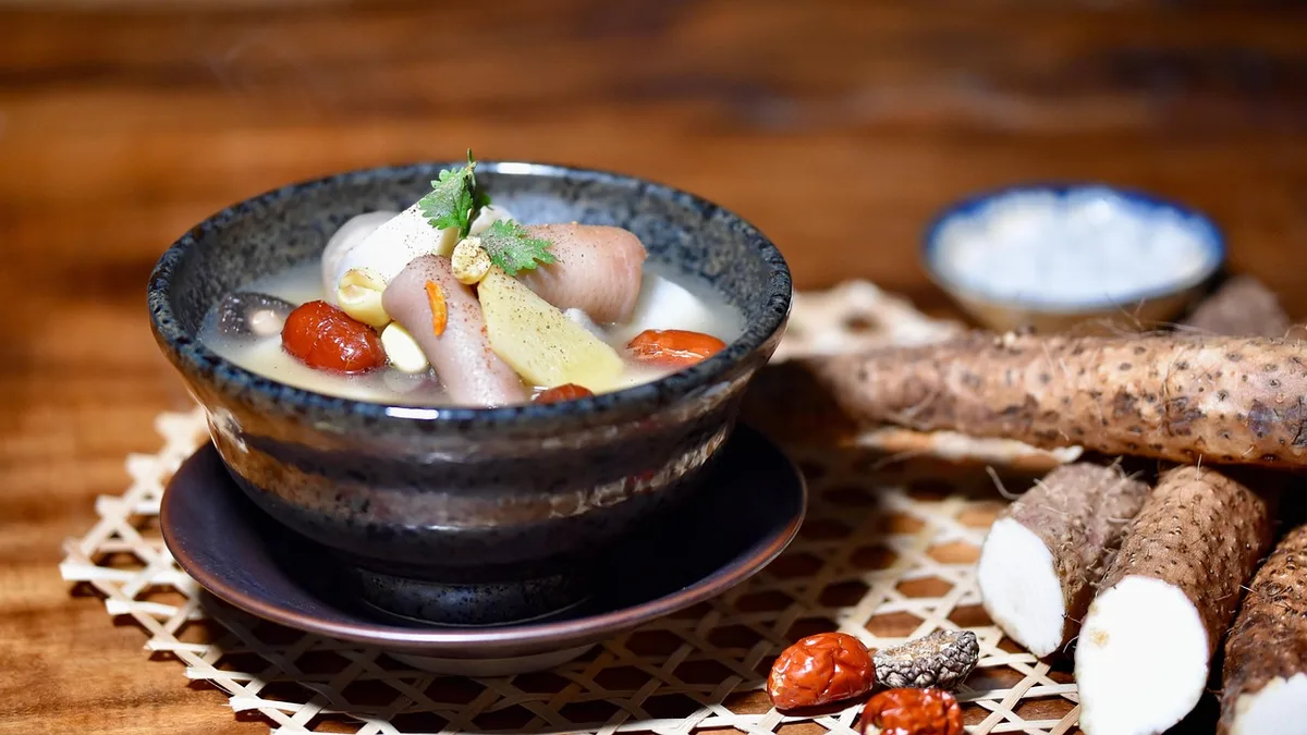 A bowl of Chinese yam soup with red dates, whole yam roots on the table beside it