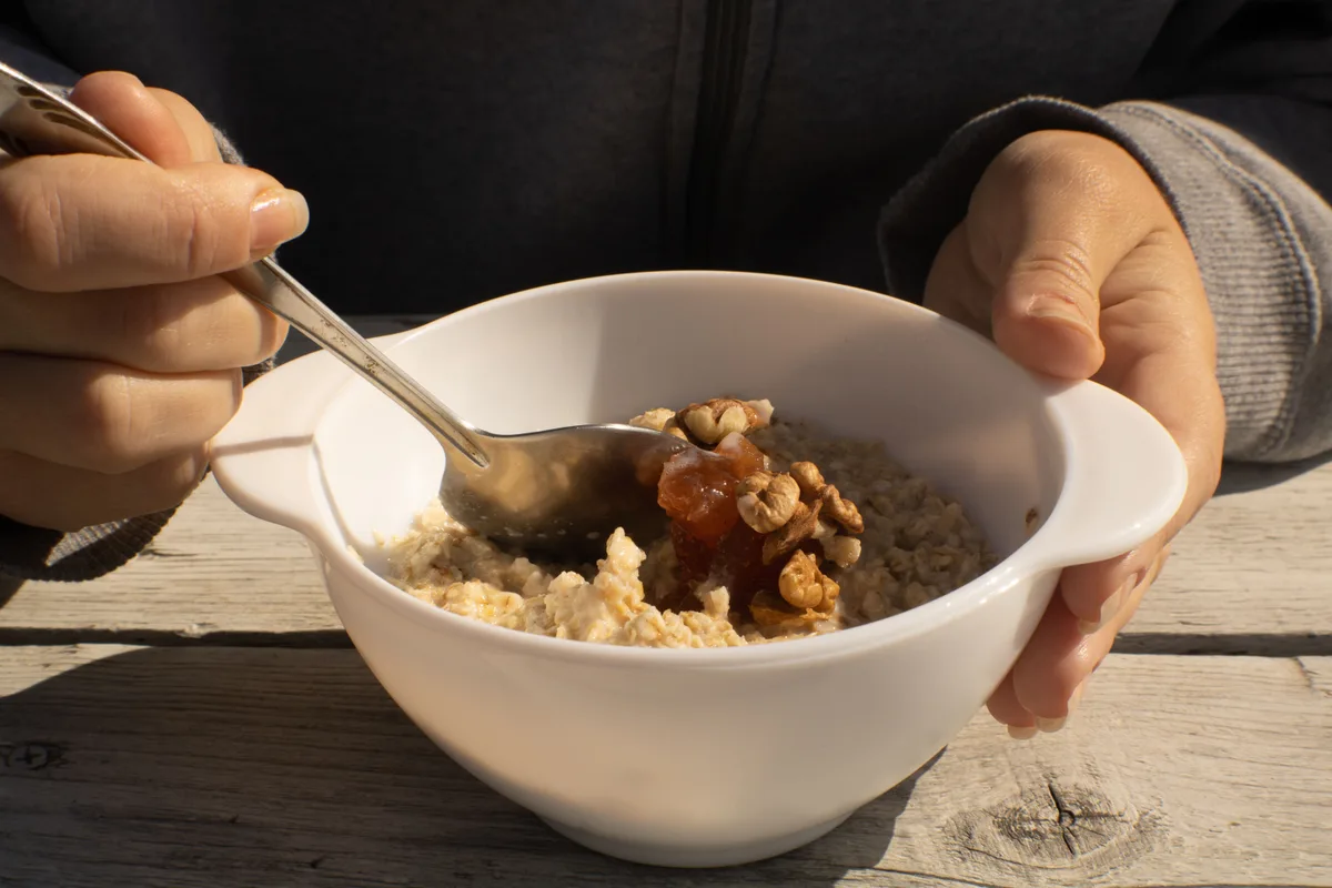 Hands holding a bowl of warm oatmeal topped with walnuts