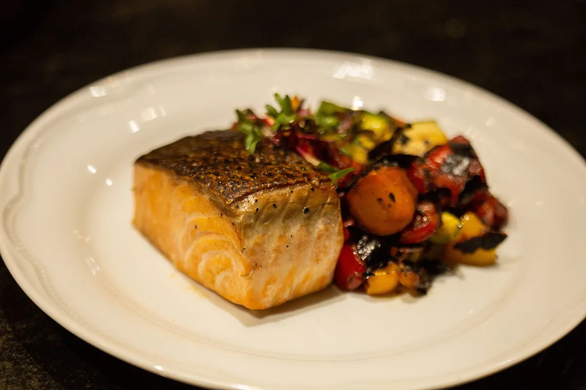 A seared salmon fillet with roasted vegetables on a white plate
