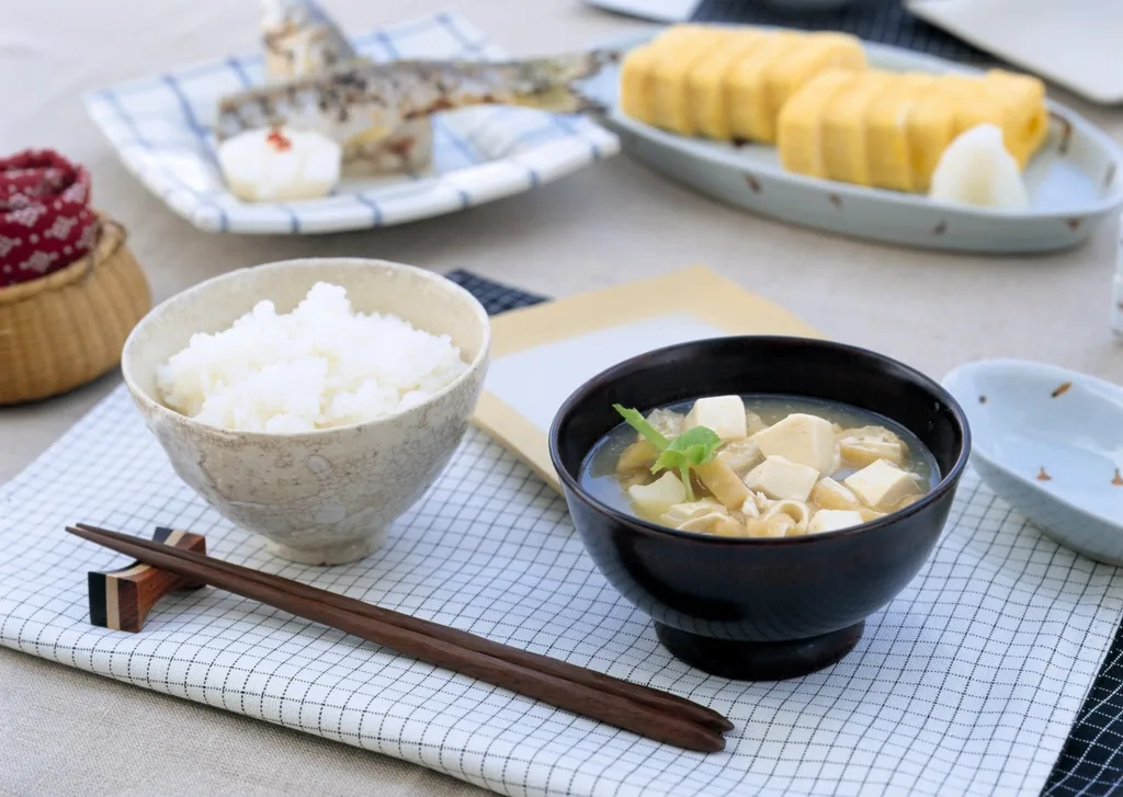 A simple Japanese meal of miso soup with tofu, a bowl of rice, grilled fish and rolled omelet