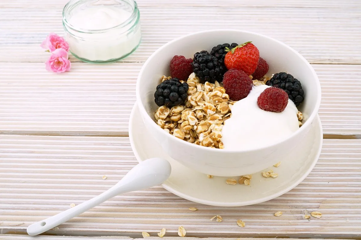 A white bowl of yogurt with rolled oats, raspberries, blackberries and a strawberry