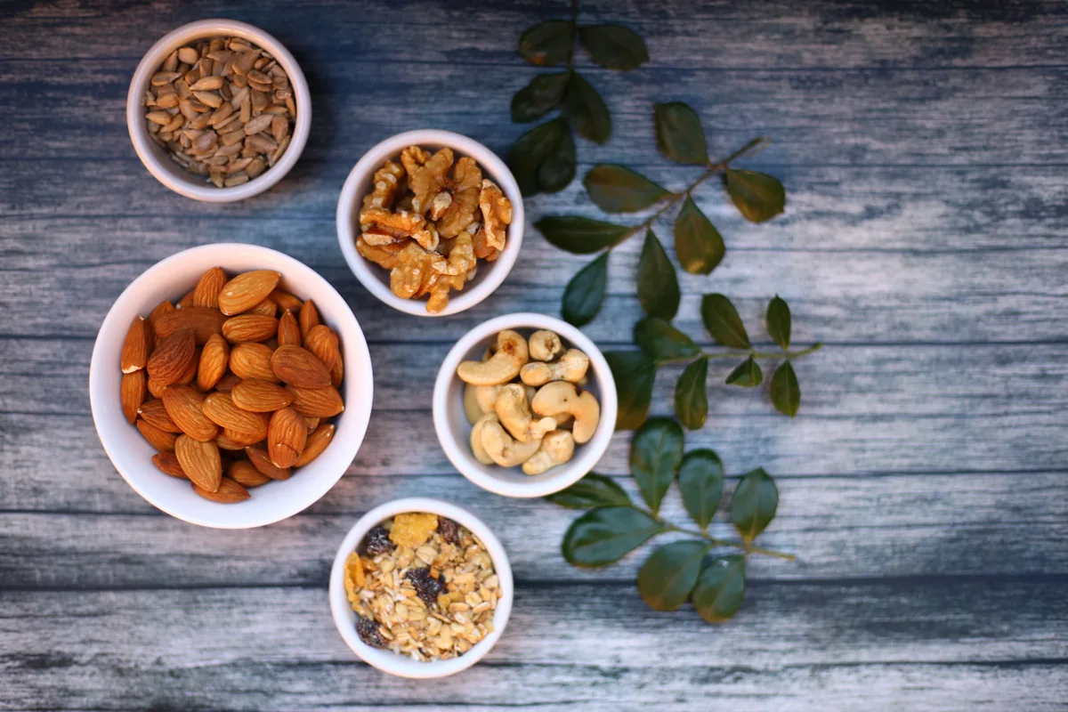 Small bowls of almonds, walnuts, cashews, sunflower seeds and granola on a blue wooden table