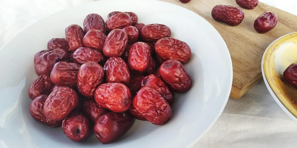A white plate piled with dried red jujubes, a few more scattered on a cutting board