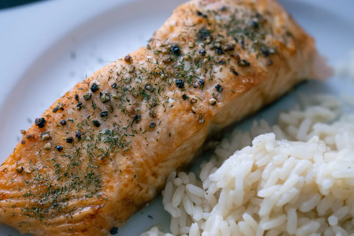 A cooked salmon fillet seasoned with herbs and cracked pepper, served with white rice