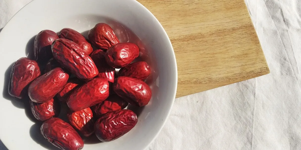 Dried red jujubes in a white bowl on a wooden board
