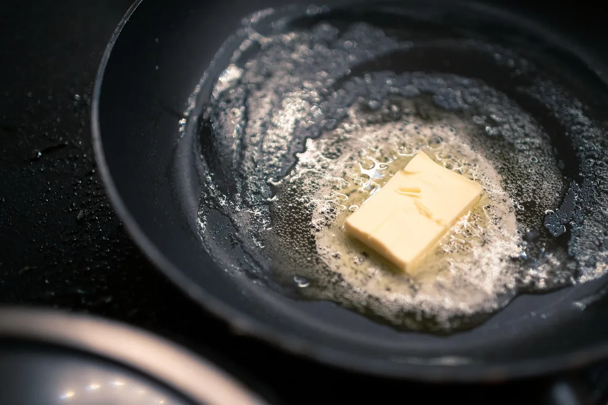 A pat of butter melting and bubbling in a dark pan