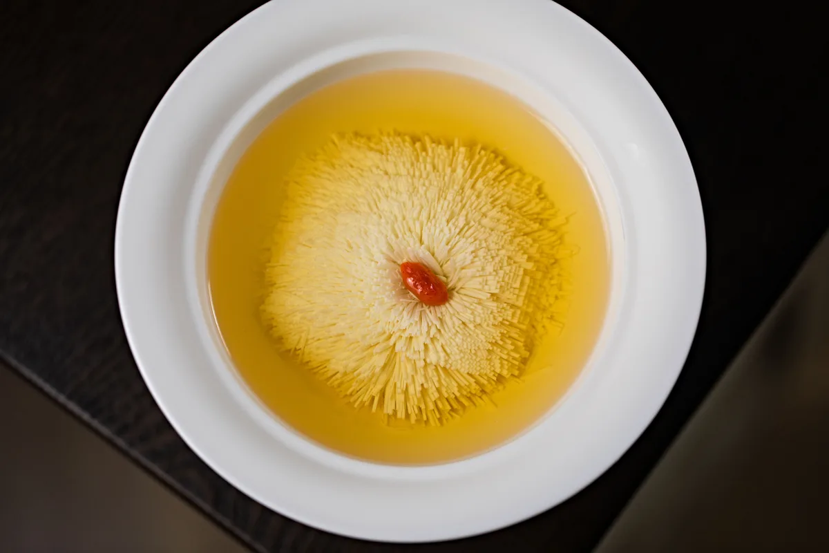 A whole chrysanthemum flower opening in a white bowl of golden tea