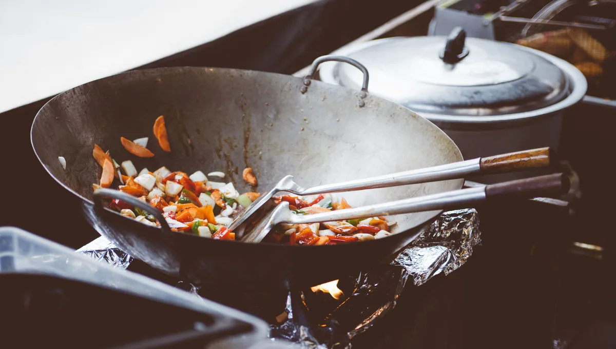 Diced vegetables cooking in a wok, with a long ladle and spatula resting inside