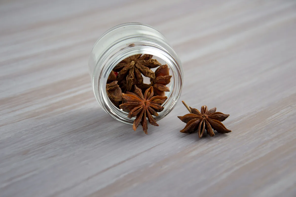 Star anise pods tipping out of a small glass jar
