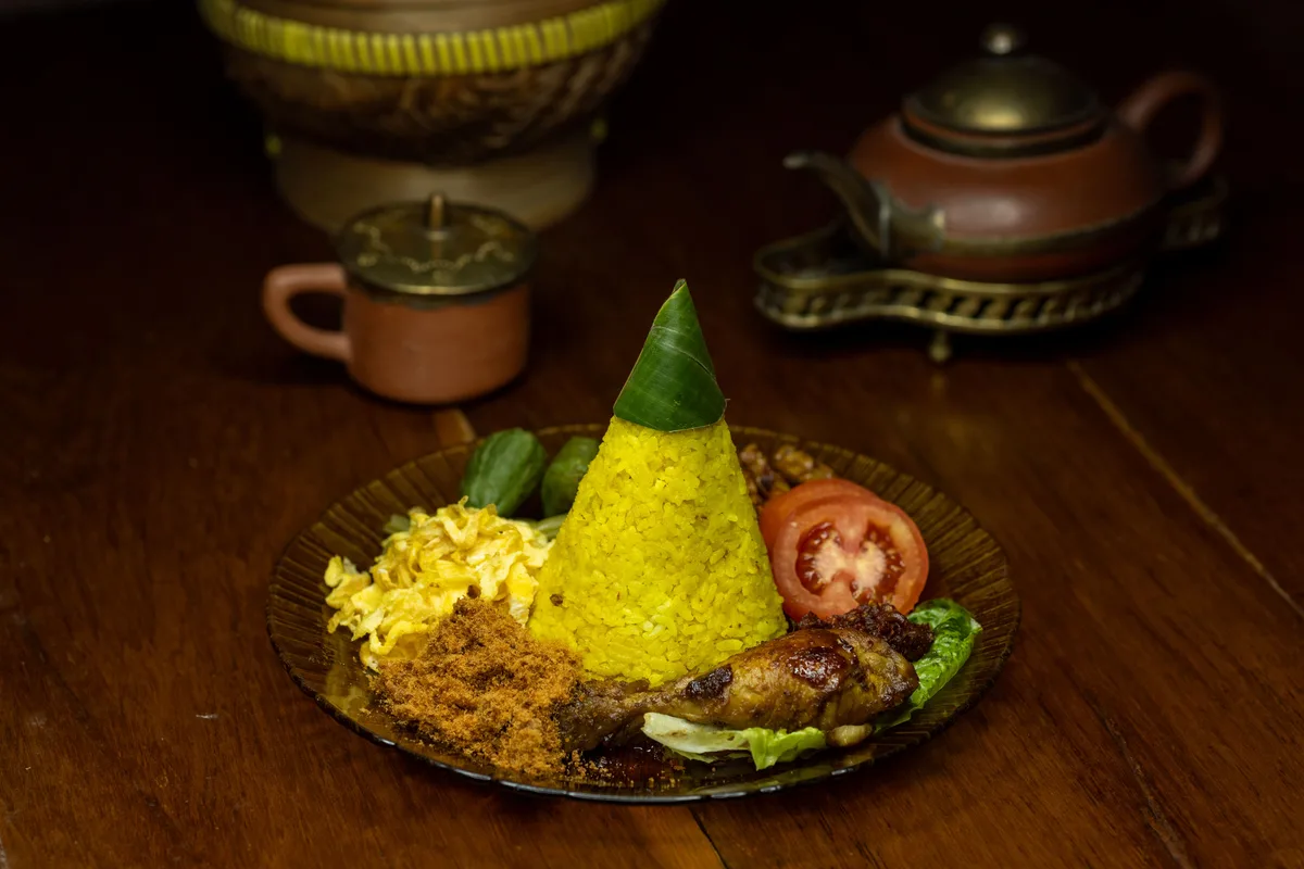 A cone of yellow turmeric rice, the Indonesian dish nasi tumpeng, served with fried chicken and sides