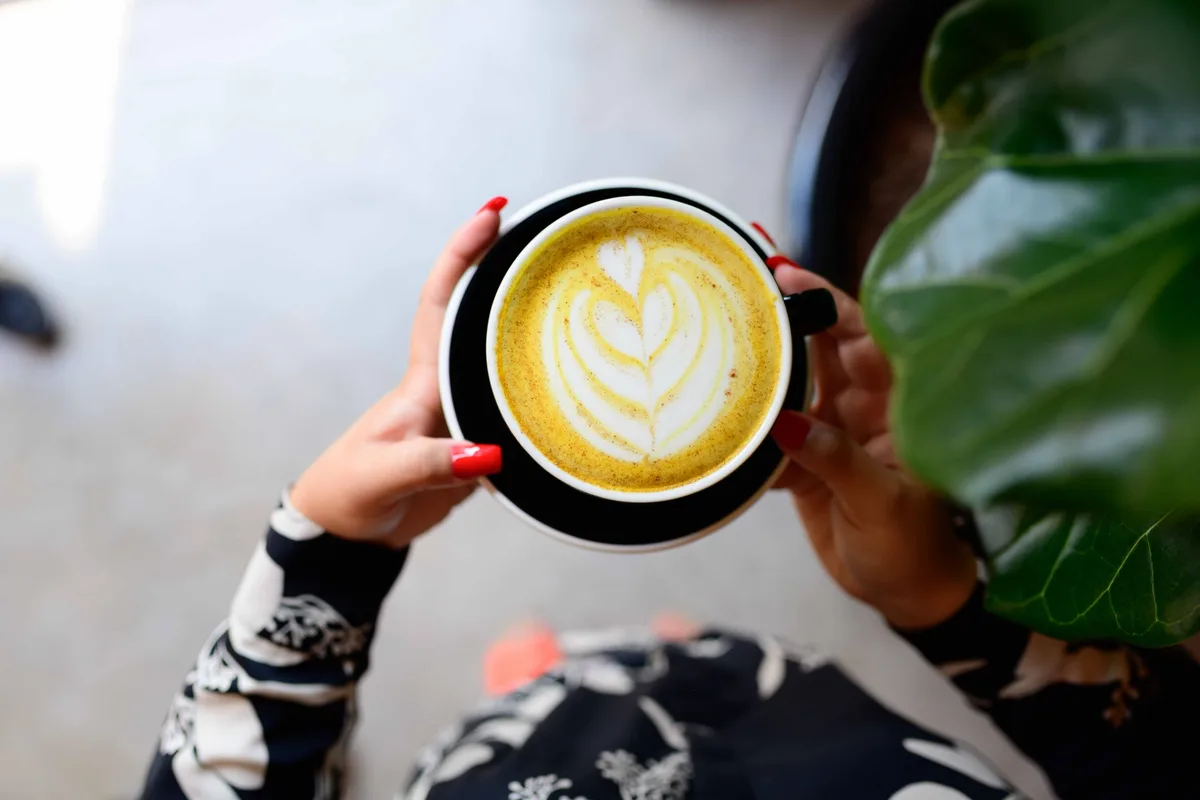 Hands holding a golden turmeric latte with a leaf pattern in the foam