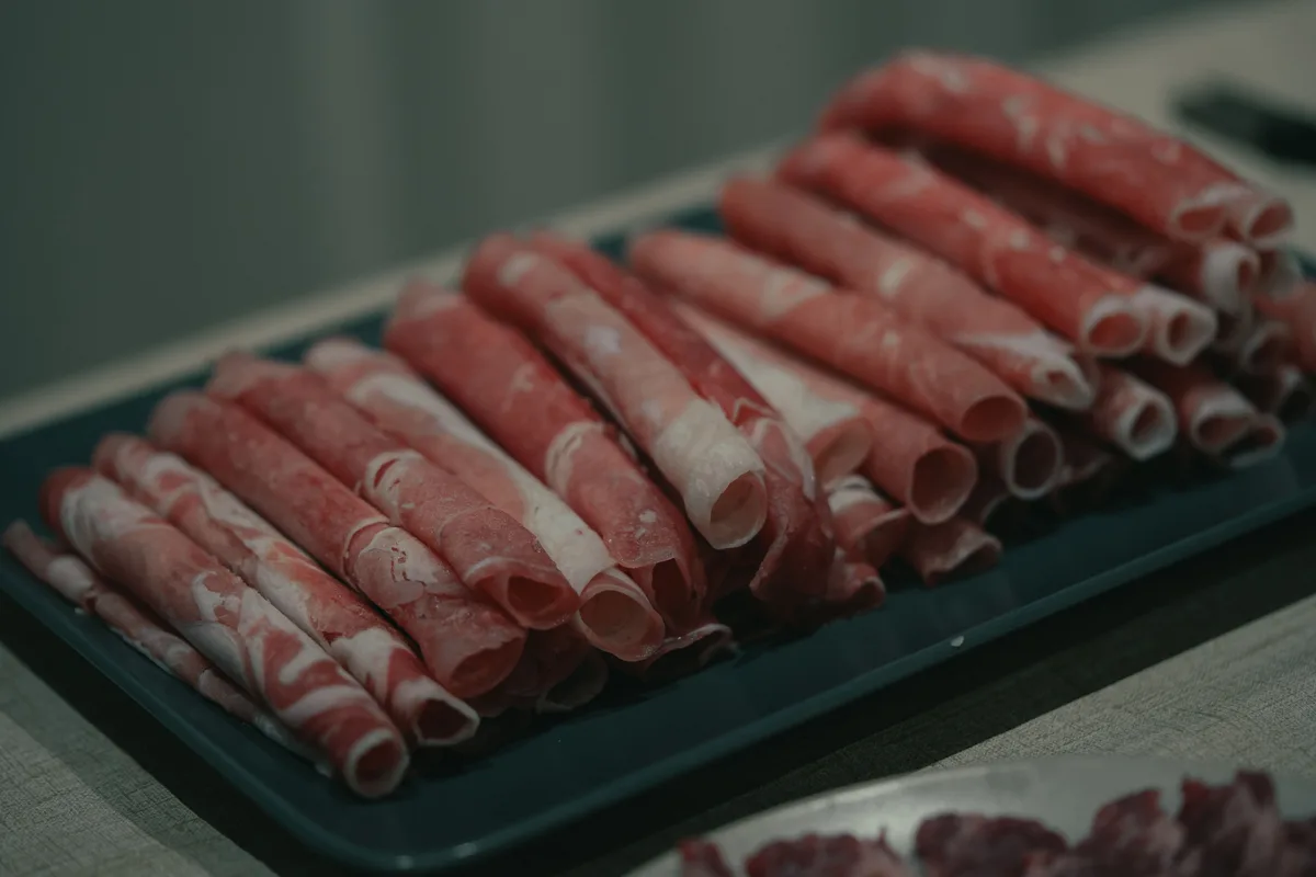 Rolls of paper thin sliced meat lined up on a tray, ready for the pot