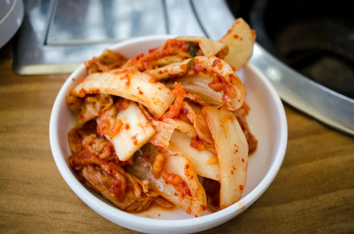 A white bowl of napa cabbage kimchi on a wooden table