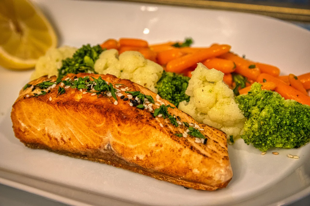 A seared salmon fillet sprinkled with sesame seeds, served with carrots, cauliflower and broccoli
