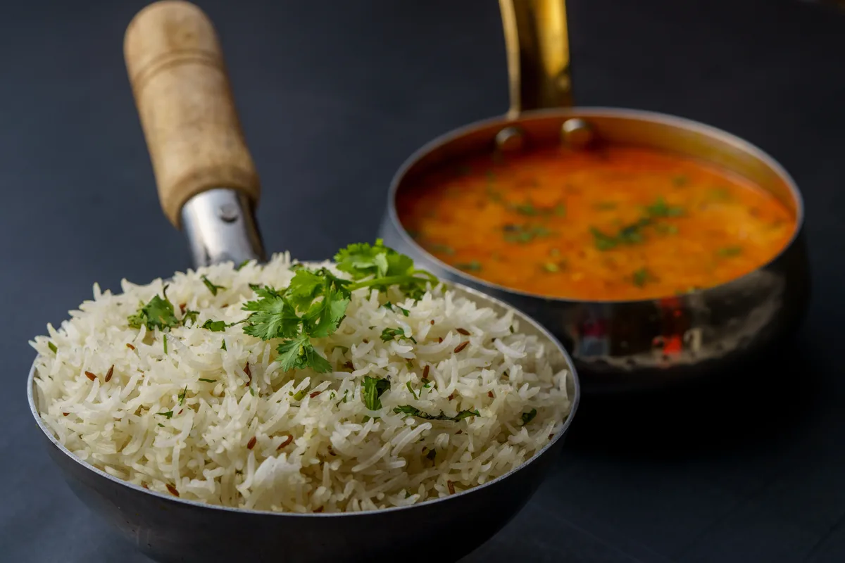 A pan of cumin rice topped with coriander, with a pot of yellow dal behind it