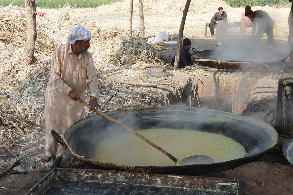 A man stirs boiling sugarcane juice in a wide iron pan, the first stage of making jaggery