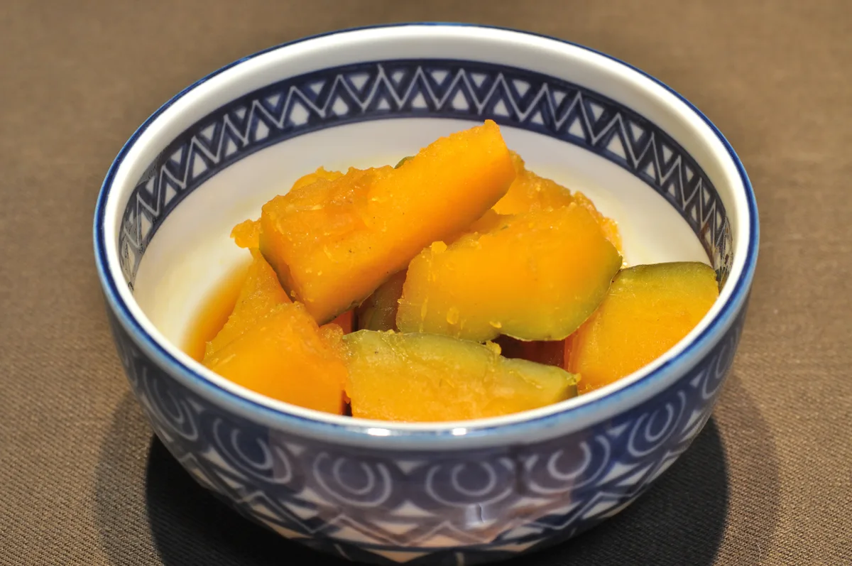 Simmered kabocha squash in a blue and white bowl, glossy with its cooking liquid