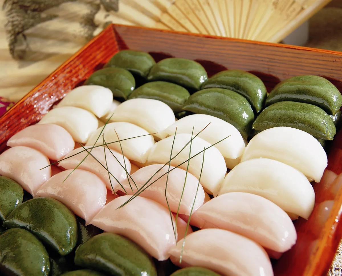 Songpyeon, half-moon rice cakes in white, pink and green, laid on a tray with pine needles