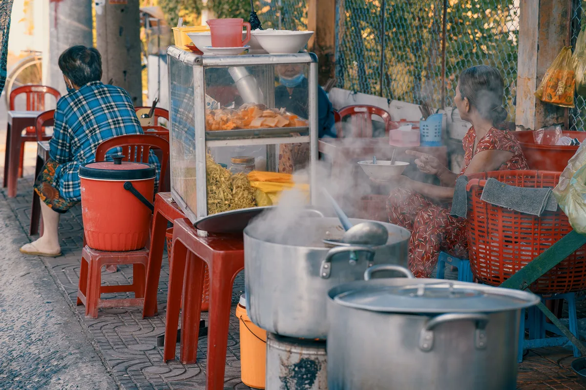 Steam rises from big covered pots at a street food stall in Vietnam