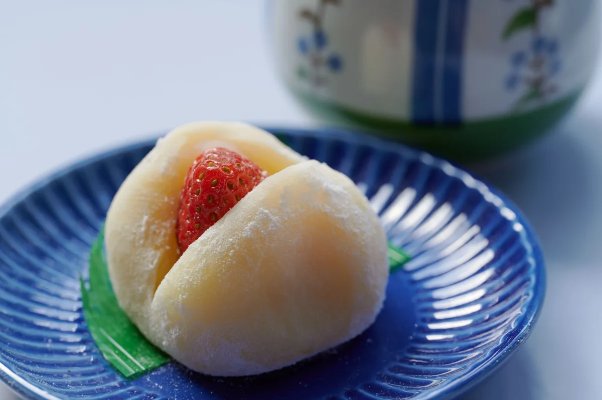 A strawberry daifuku on a blue plate, the berry showing through a split in the soft mochi