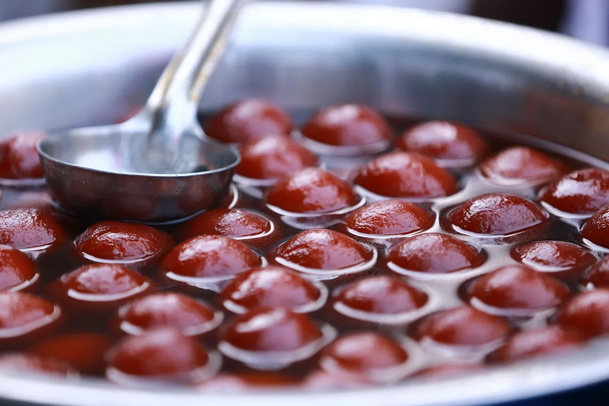 Gulab jamun soaking in sugar syrup, with a ladle resting in the pan