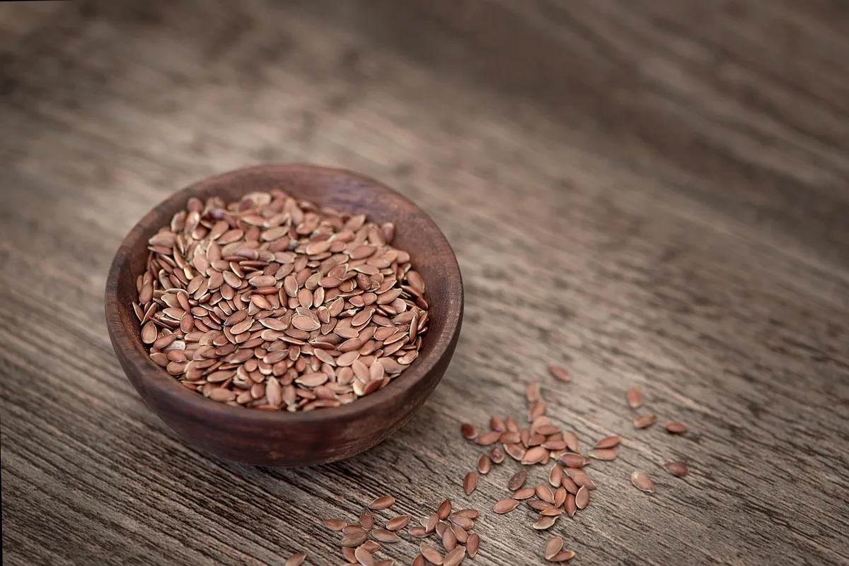 A wooden bowl of brown flaxseed on a rustic table