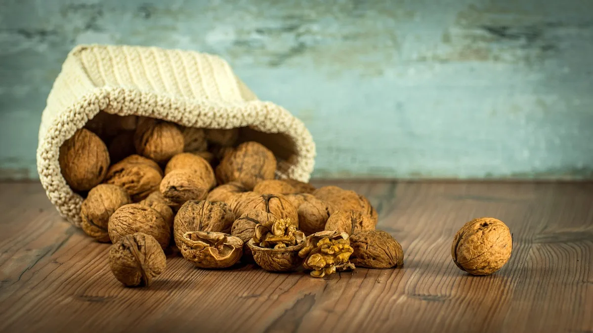 Whole and cracked walnuts spilling from a knitted sack onto a wooden table