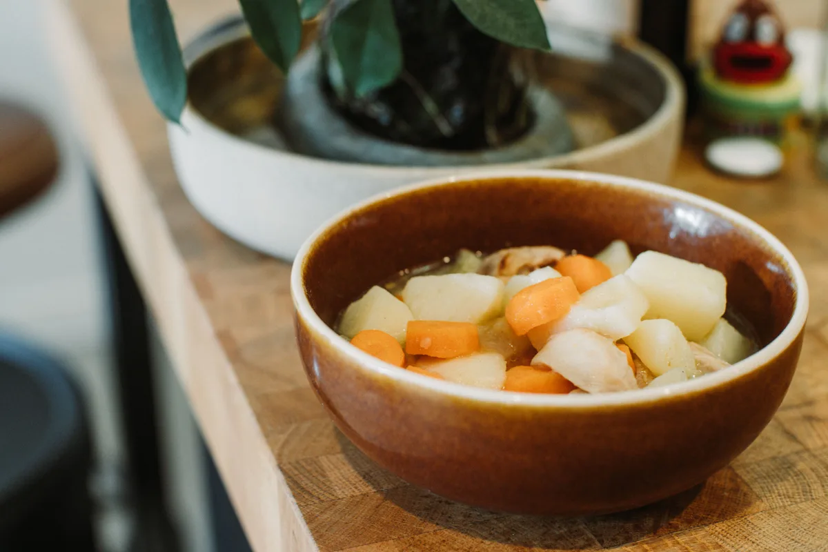 A brown ceramic bowl of stew with chunks of carrot and other root vegetables