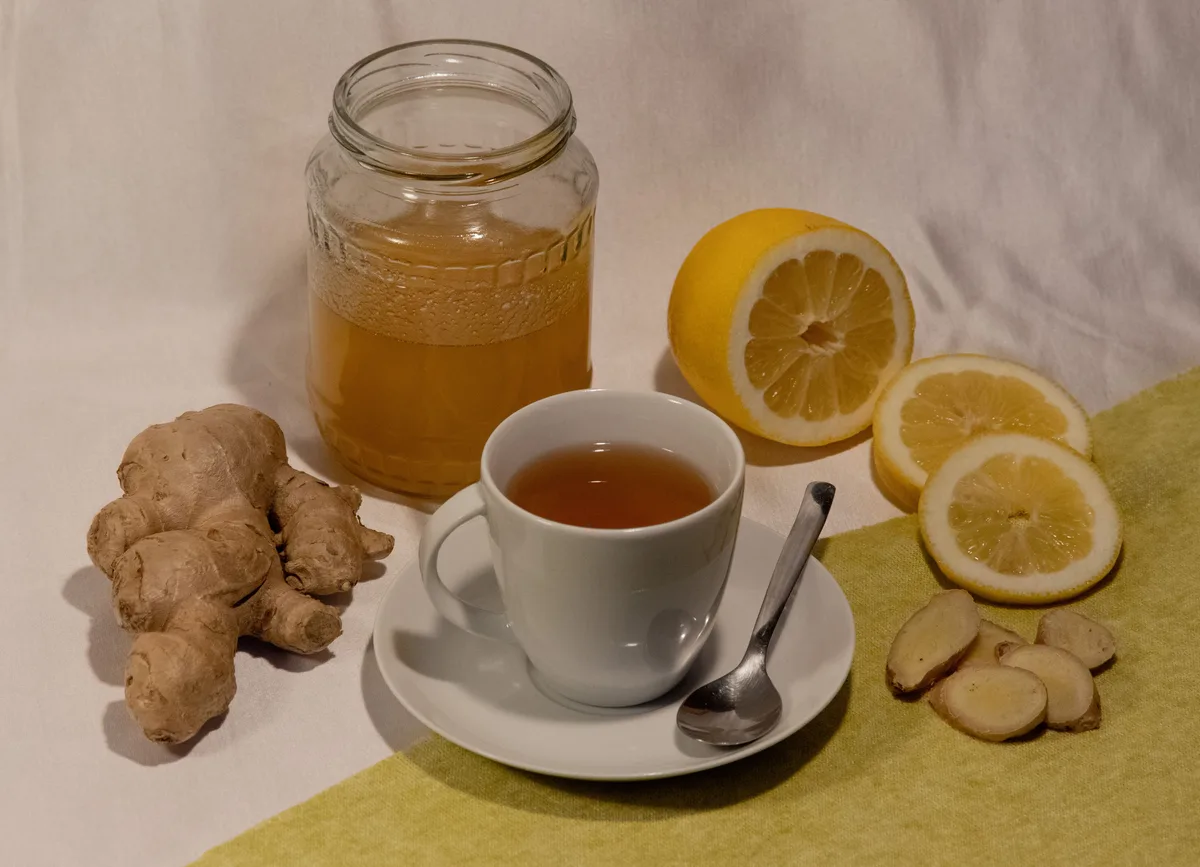 A cup of tea with fresh ginger root, lemon slices and a jar of honey