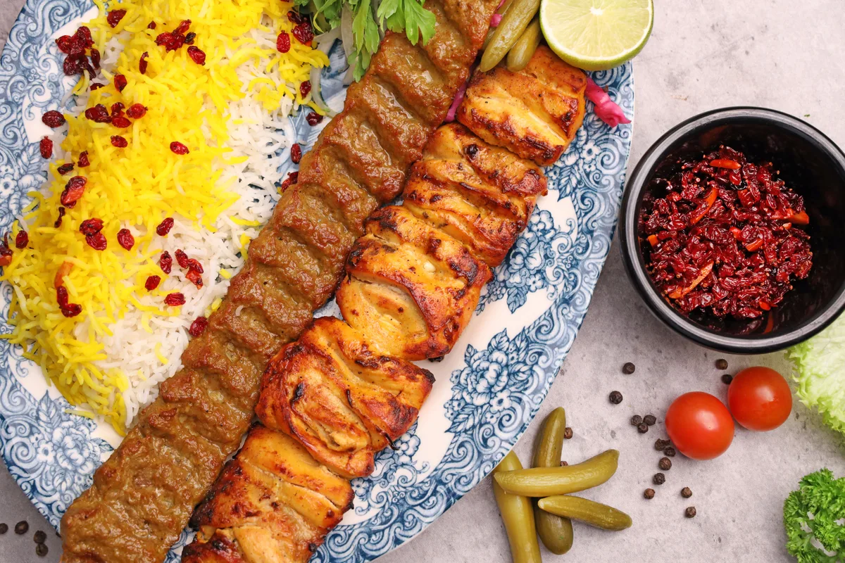 Persian saffron rice topped with barberries, served with two kinds of kebab on a patterned platter