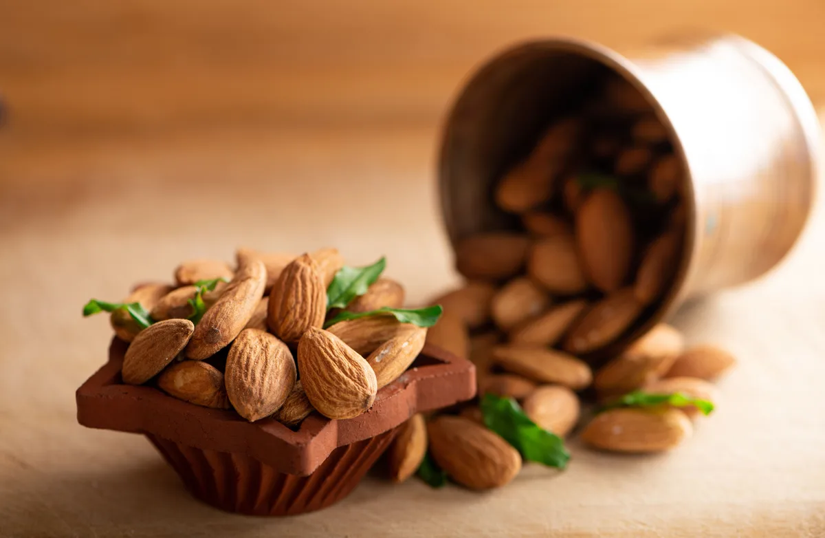 Almonds spilling from a copper cup onto a small dish