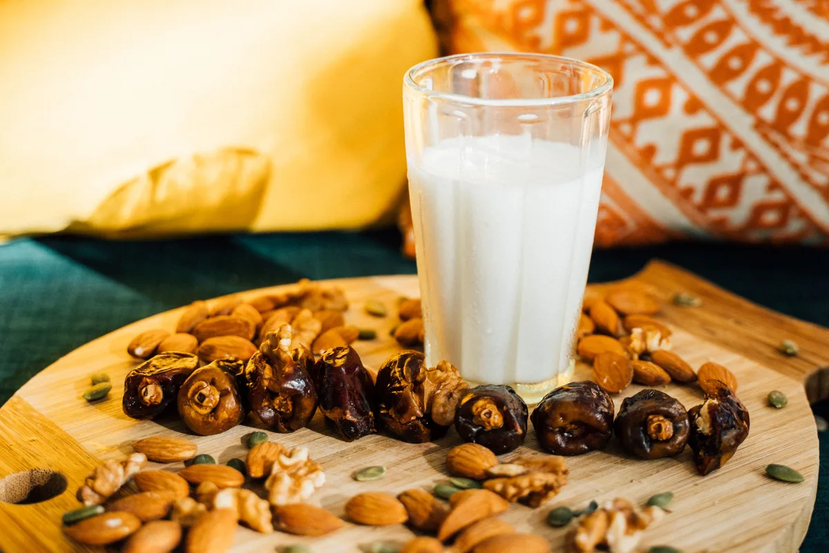 A glass of milk on a wooden board scattered with dates and almonds