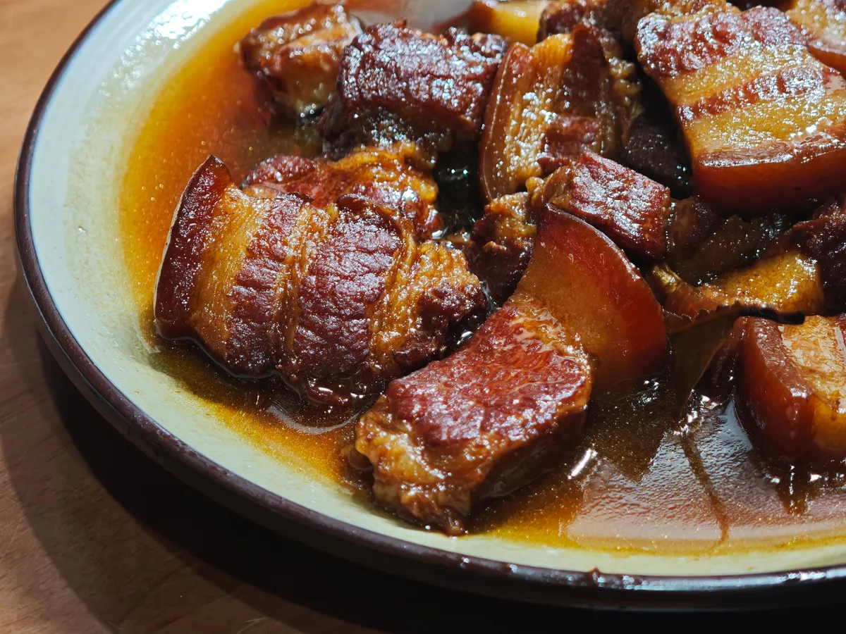 Red braised pork belly, glossy and deep mahogany brown, in a shallow bowl