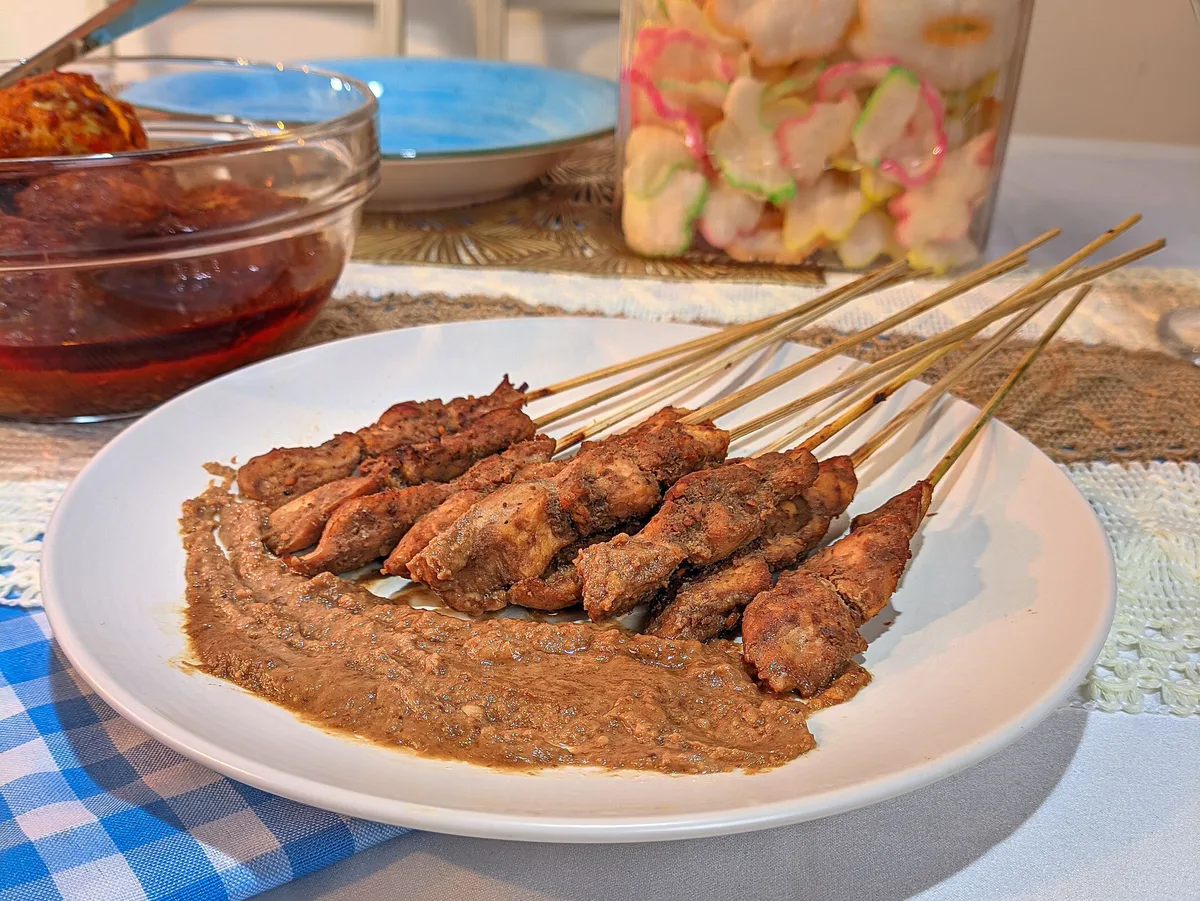 Indonesian satay skewers on a white plate over a bed of peanut sauce