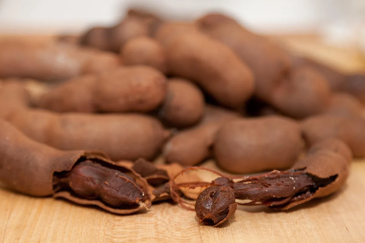Tamarind pods on a wooden board, one cracked open to show the sticky brown pulp