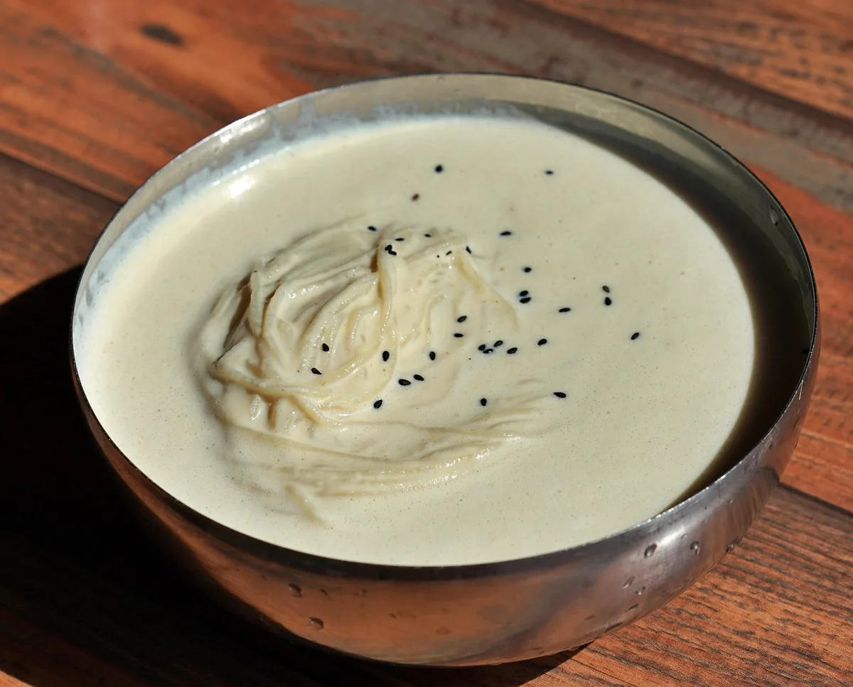 Kongguksu, thin noodles in a pale cold soy milk broth with black sesame seeds, in a metal bowl