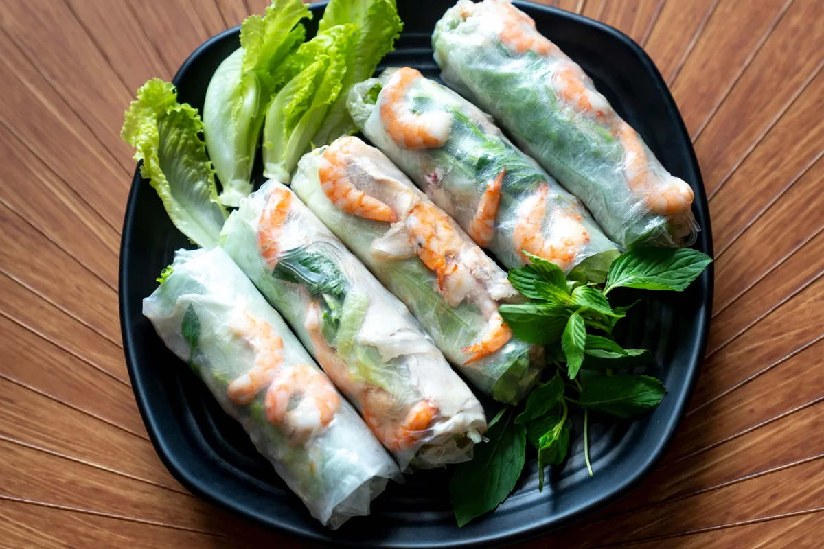 Vietnamese rice paper rolls filled with shrimp, herbs and lettuce on a black plate