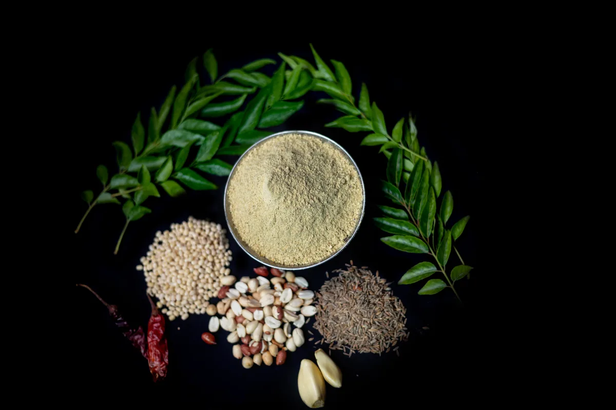 Sprigs of fresh curry leaves around small piles of seeds, a dried chili and garlic