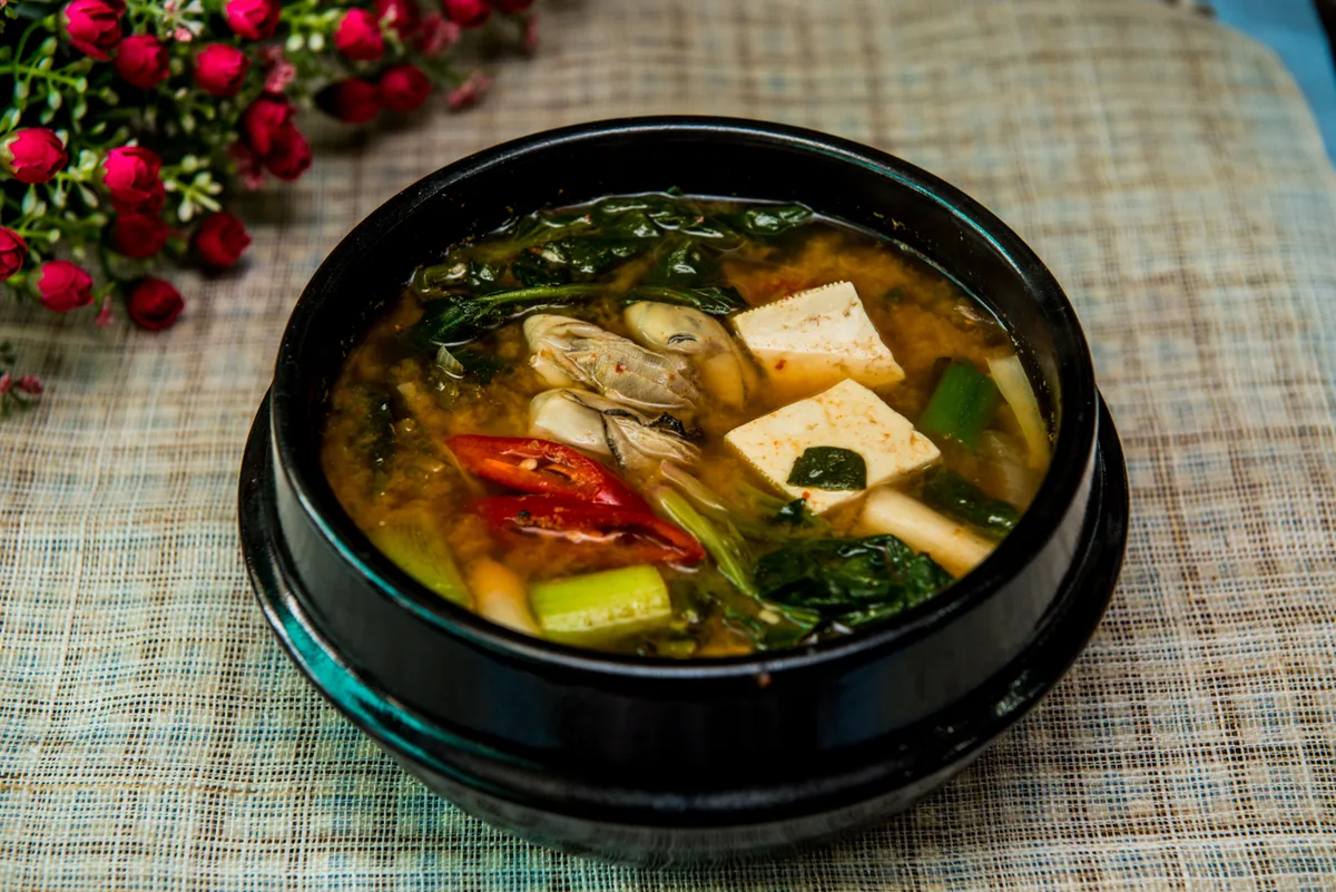 Doenjang jjigae in a black earthenware pot, with tofu, vegetables and sliced red chilli